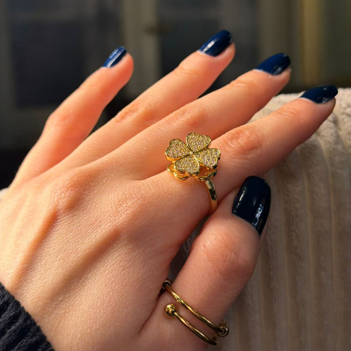 Hand wearing a gold ring with a diamond-like stone against a blurred background