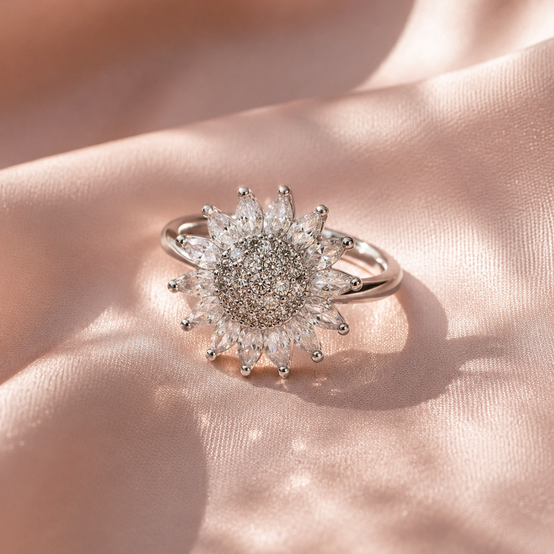 A silver sunburst ring with clear marquise-cut and round gemstones, resting on draped light pink satin fabric.