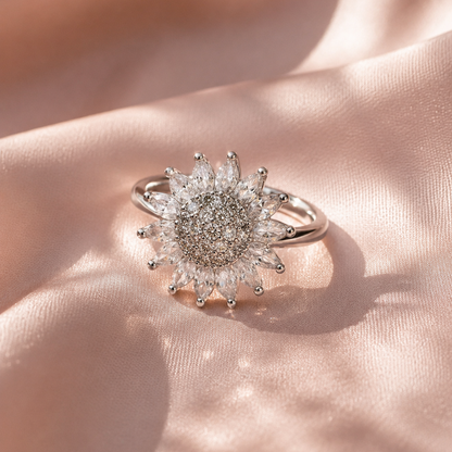 A silver sunburst ring with clear marquise-cut and round gemstones, resting on draped light pink satin fabric.
