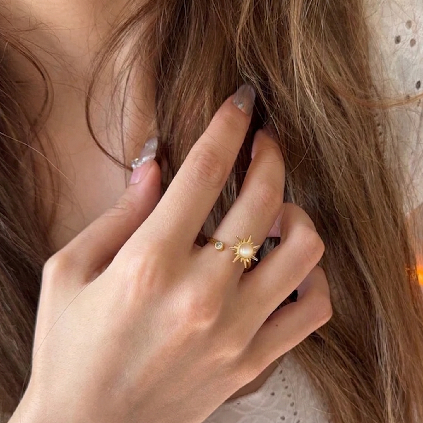 Close-up of a hand with a gold ring featuring a sun design, touching hair.