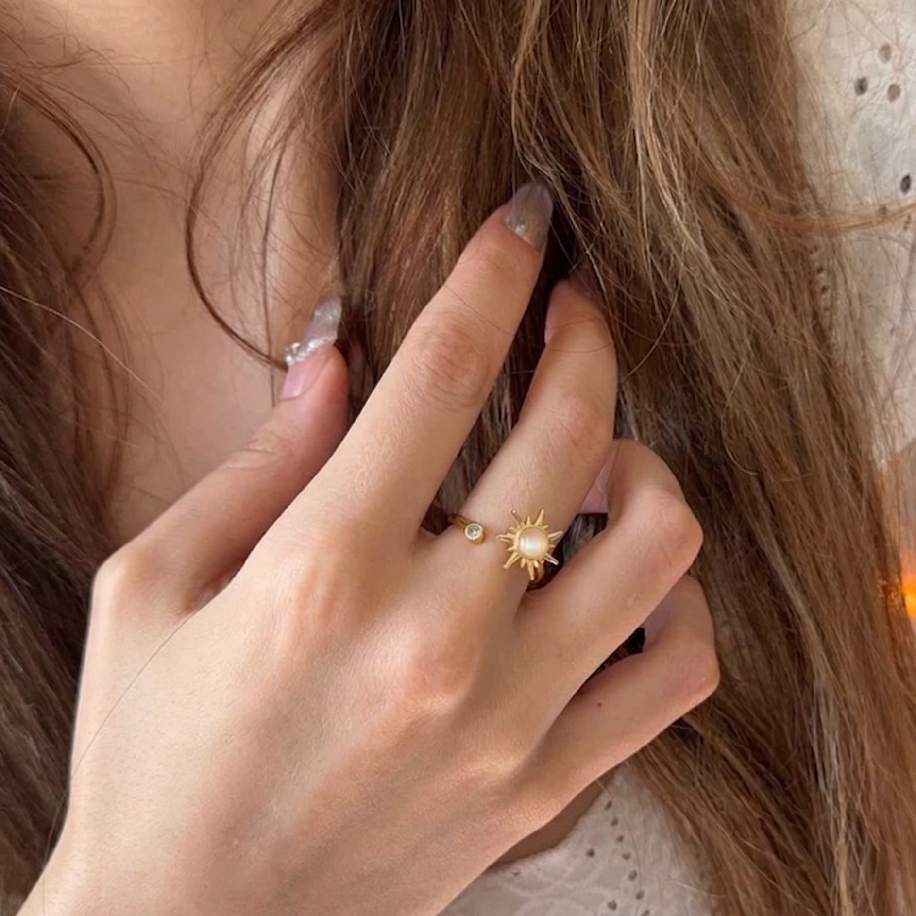 Close-up of a hand with a gold ring featuring a sun design, touching hair.