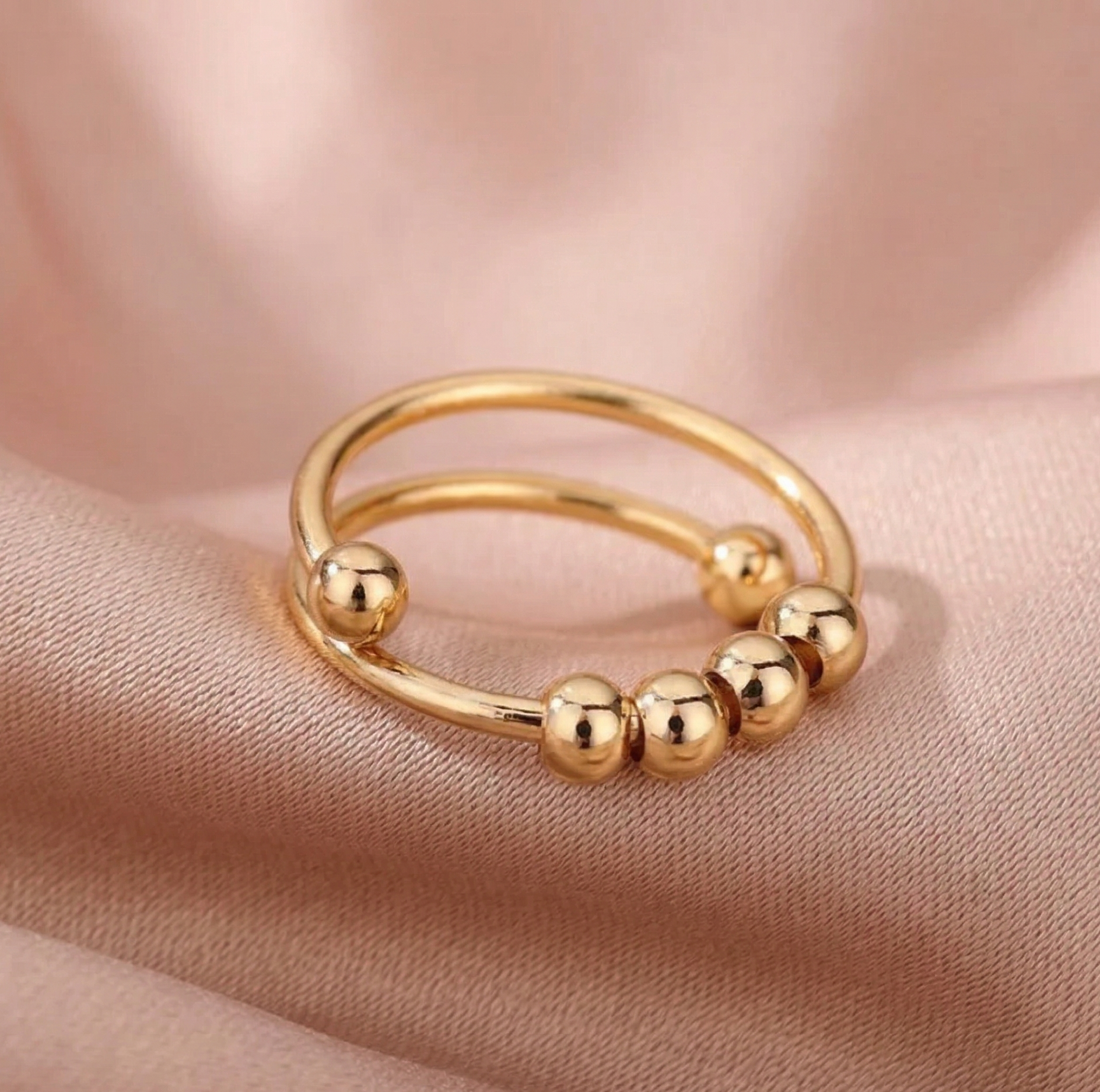Gold ring with bead accents on a soft pink fabric background