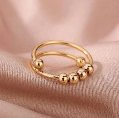 Gold ring with bead accents on a soft pink fabric background