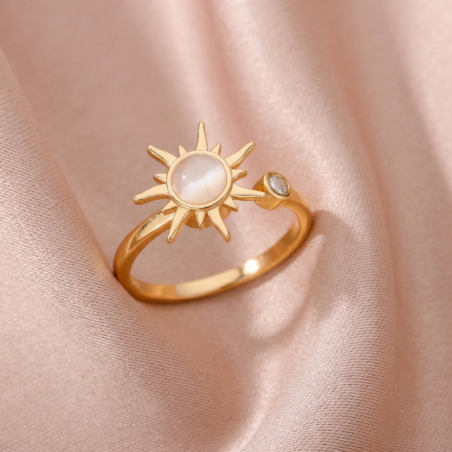 Gold ring with sun design on a soft pink fabric background