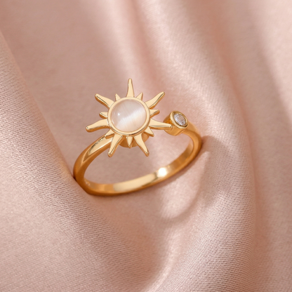 Gold ring with sun design on a soft pink fabric background